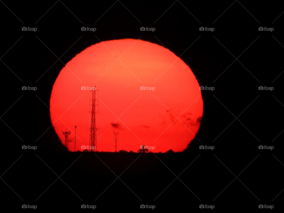 Big, red, descending sunset over the antenna farm. Antennas are silhouetted in the background