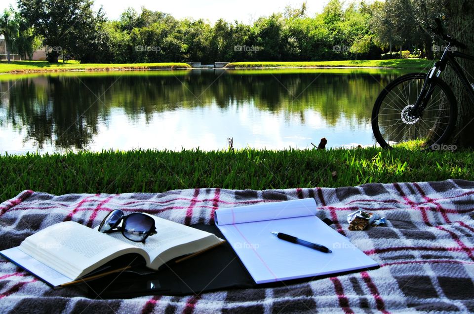 Sunglasses and book on textile near the pond