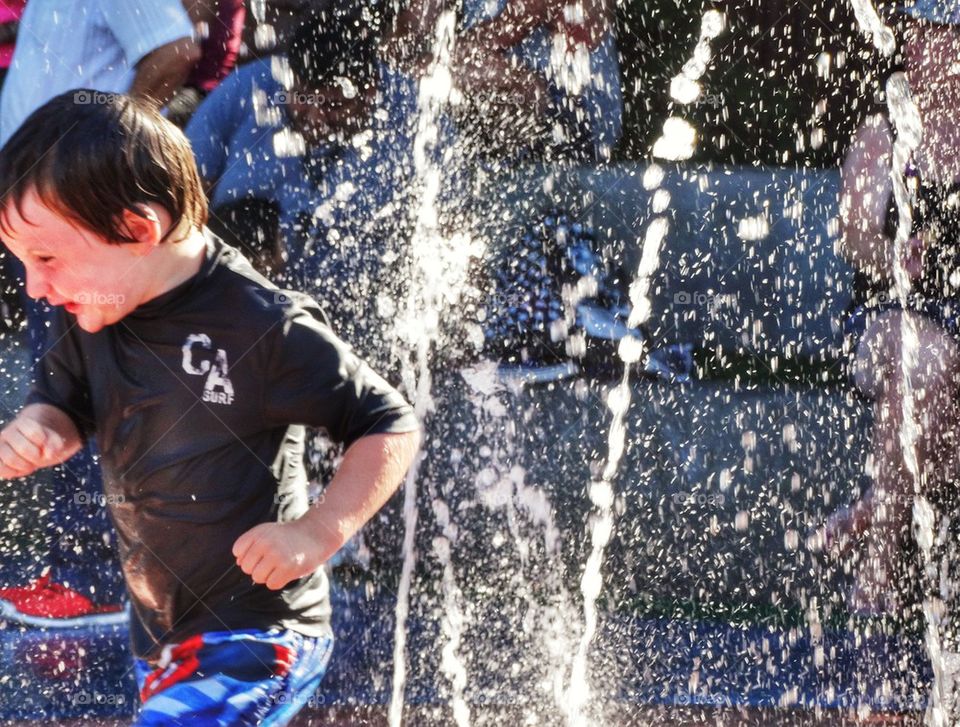 Boy Splashing In A Fountain. Cooling Off During A Heat Wave
