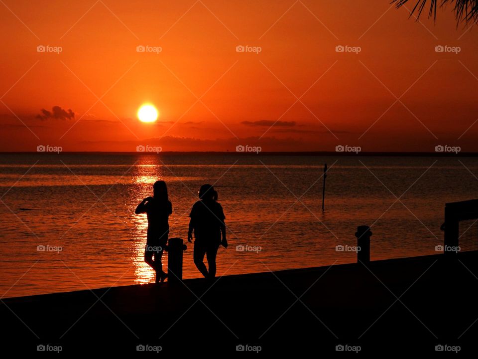 Two young ladies walking along the beach taking photos of the sunset over the Gulf of Mexico