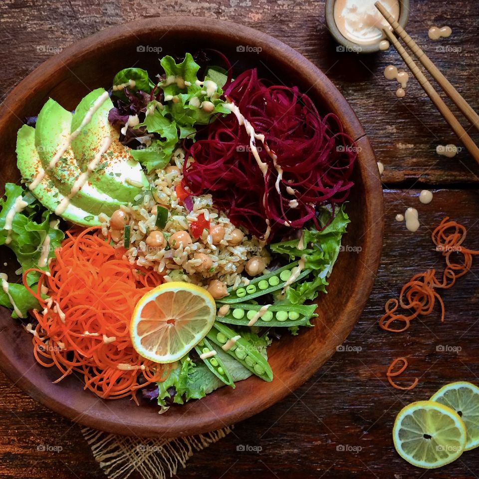 Wooden salad bowl with leafy greens, avocado, snow peas, chic peas, rice and spiraled carrots and beets.