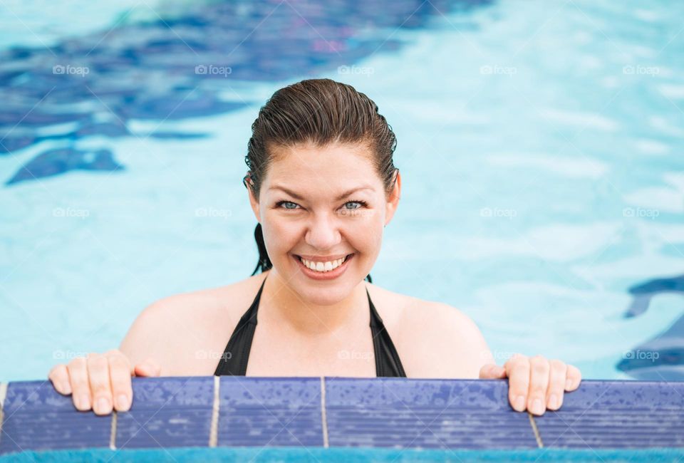Portrait of young woman plus size in black swimsuit swimming in the pool