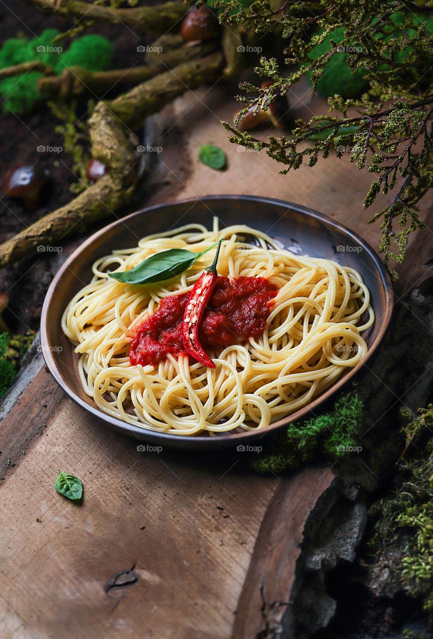 Cooked pasta in a ceramic plate with chili sauce and chili pepper in the forest 