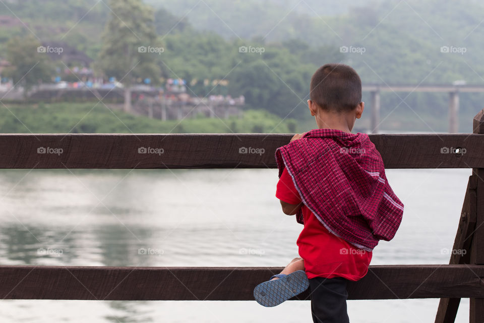 Boy looking into the river on the wood bridge