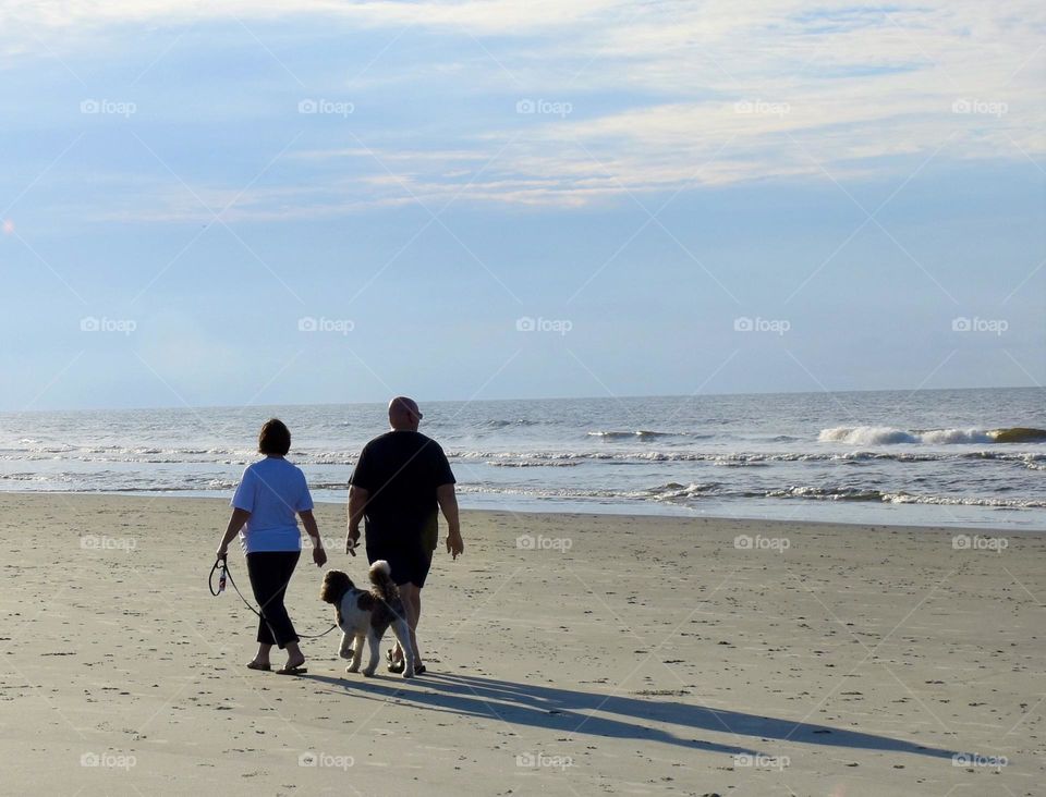 A couple walking on the beach with their dog 