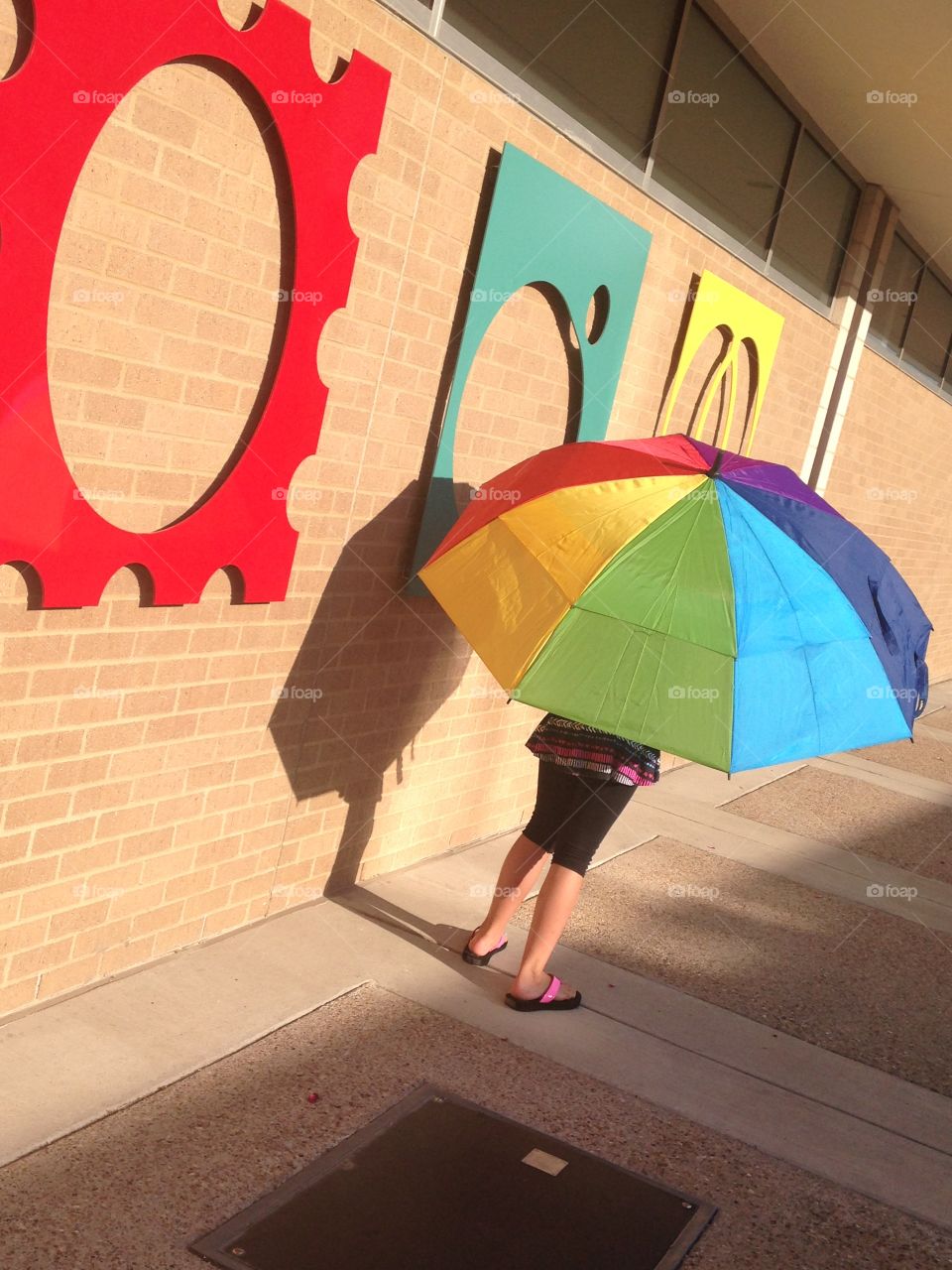 Fun with colors. Girl under rainbow umbrella next to colorful art 