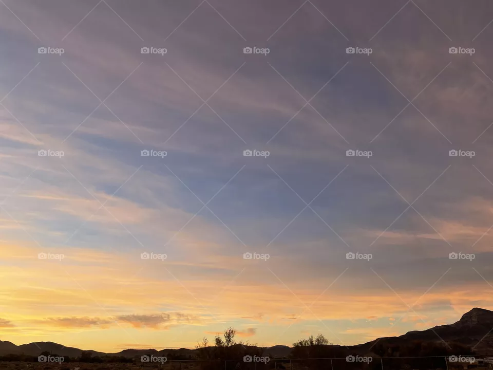 A cloudy sunset with yellow tinted clouds and mountains. 