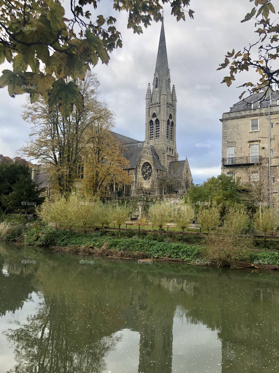 Beautiful church on the riverbank, framed with leafy green  trees on a crisp autumnal day