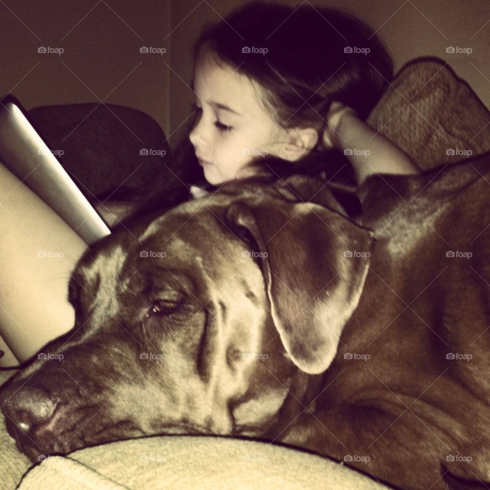 Girl's Best Friend. A young girl playing on a tablet, resting on her dog. 