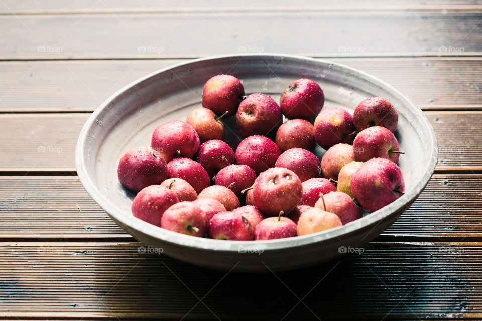 Closeup of big bowl of fresh red apples sprinkled raindrops on wooden table