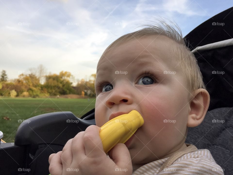 Cute baby boy entertaining himself chewing on yellow teething toy 