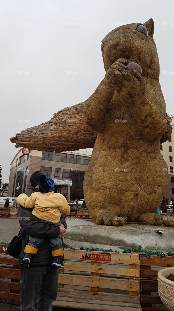 father and a son looking on a squirrel statue in Almaty