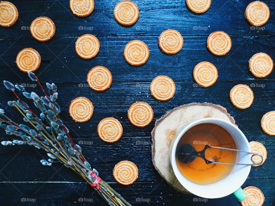 cookies, a cup of tea and willow branches on a black background