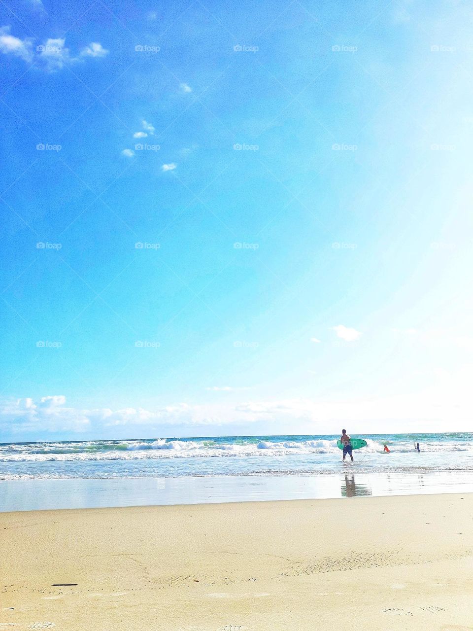 A surfer carries a surfboard into the ocean for a day of surfing at Ponce Inlet Beach in Ponce Inlet, Florida.