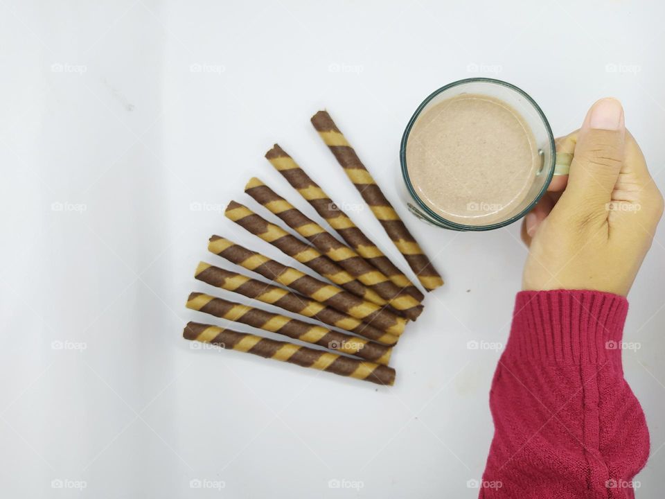 Holding a glass of chocolate milk and some wafer roll sticks on white background. Top view