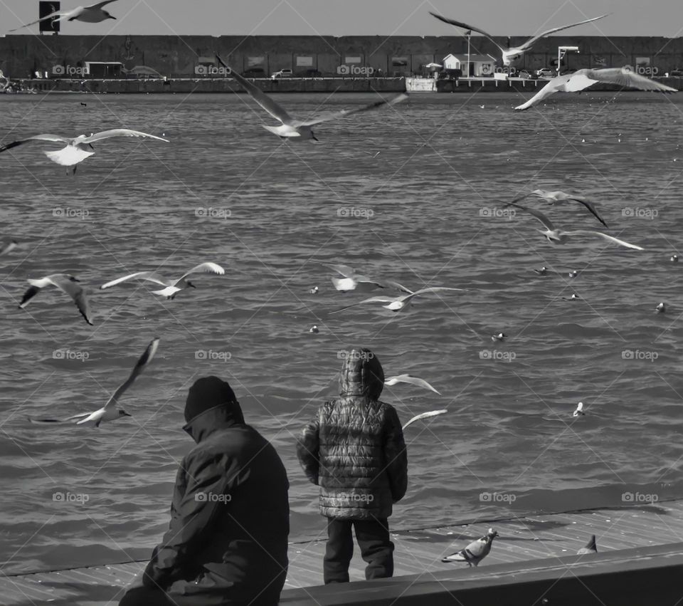 Black and white photo of a man and child is sitting near the sea