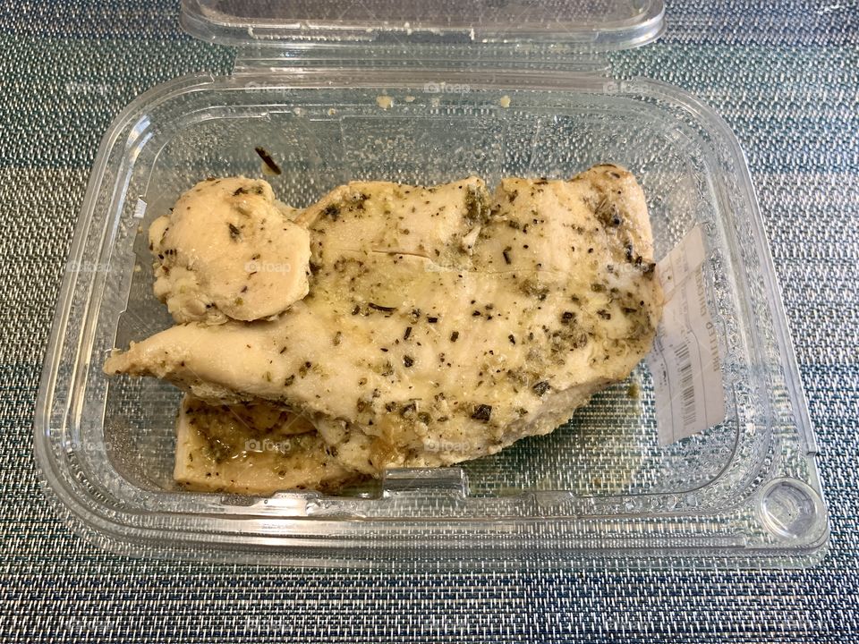 Baked chicken in an open transparent container with sky blue place mat background. Lunch and dinner.