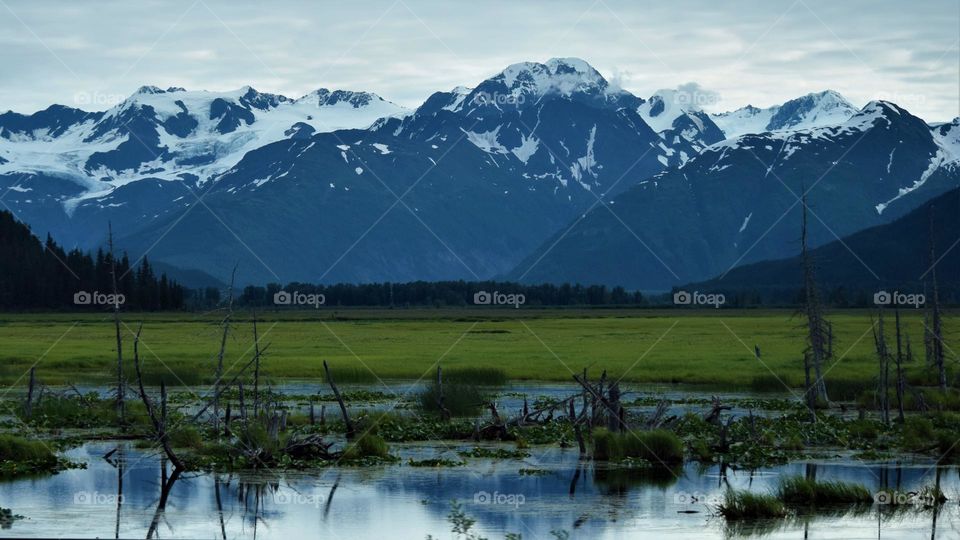 A mountain range is reflected on the surface of a calm body of water near Anchorage Alaska
