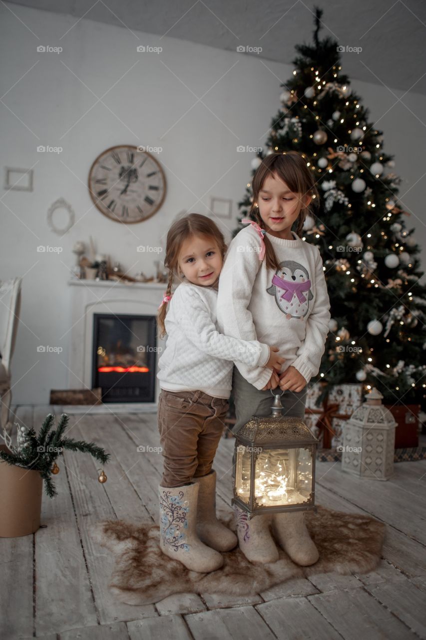 Little sisters near Christmas tree at home