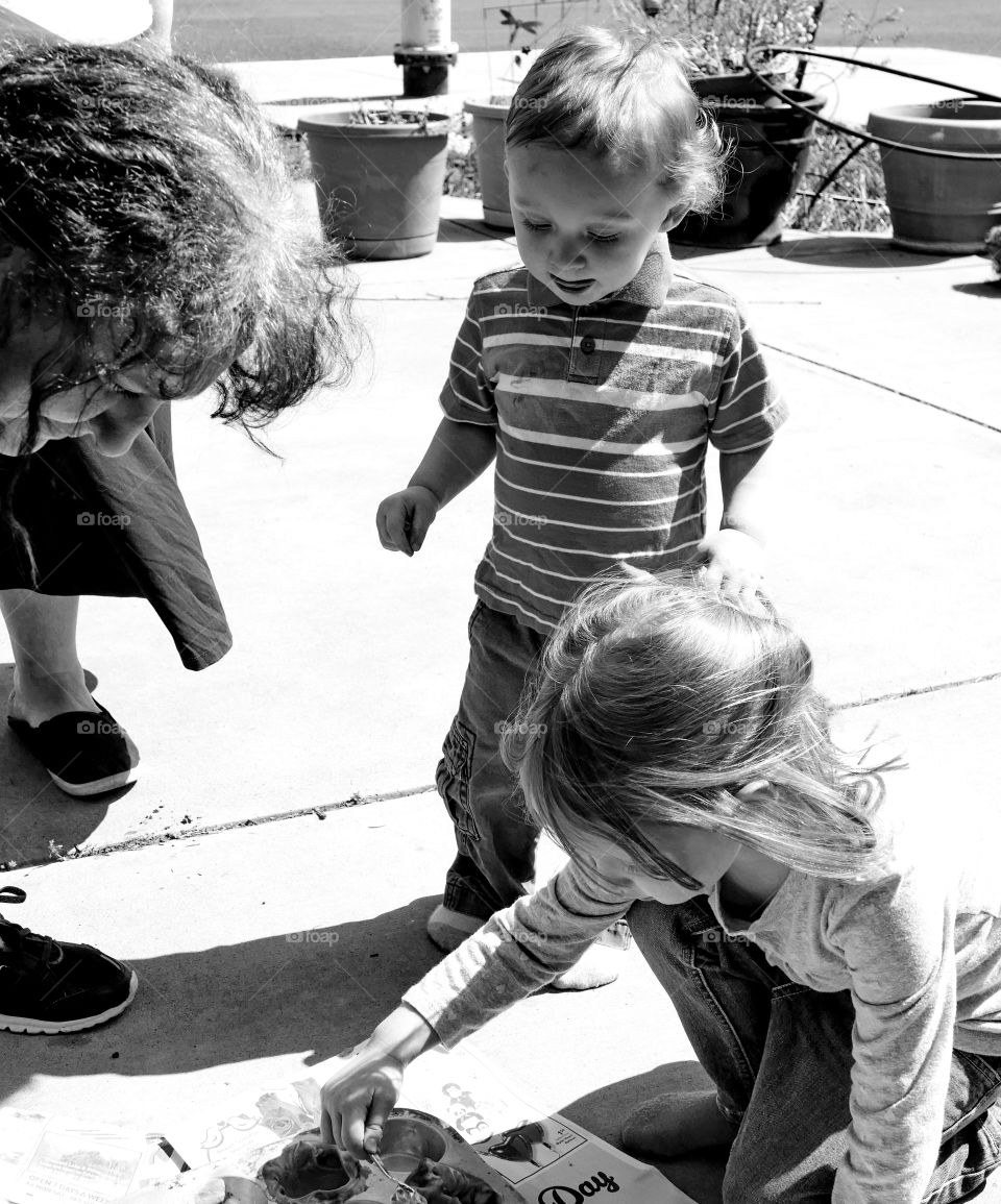 A family including a grandma, young toddler boy, and young girl having fun coloring Easter eggs together. 