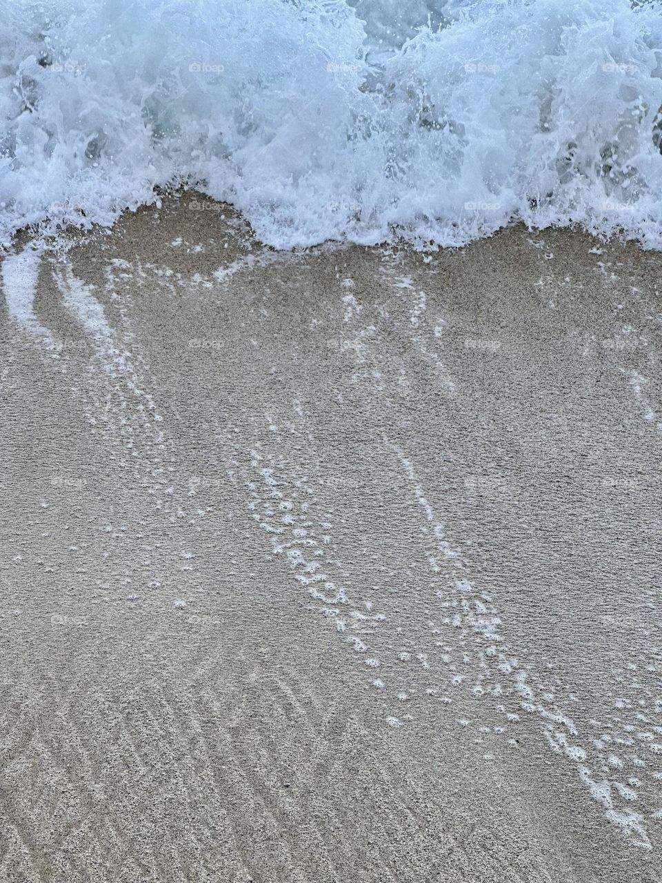 The moon’s gravity pulls the Earth’s oceans tides, as waves endlessly wash up the beach and back down - Pacific Ocean on Hawaii sand