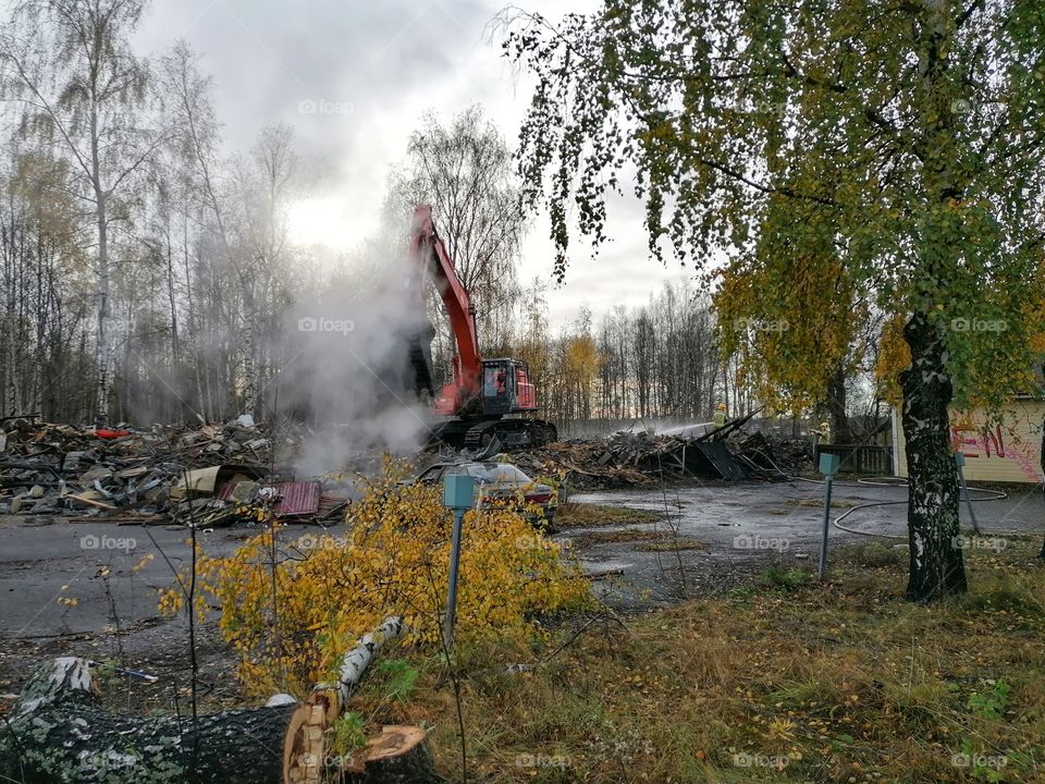 A firefighter and an excavator extinguishing a fire in a large building.