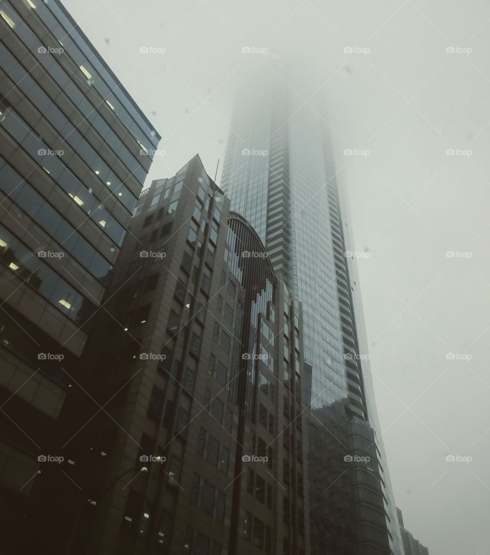 Large buildings surrounded by fog and the tops are disappearing into the sky