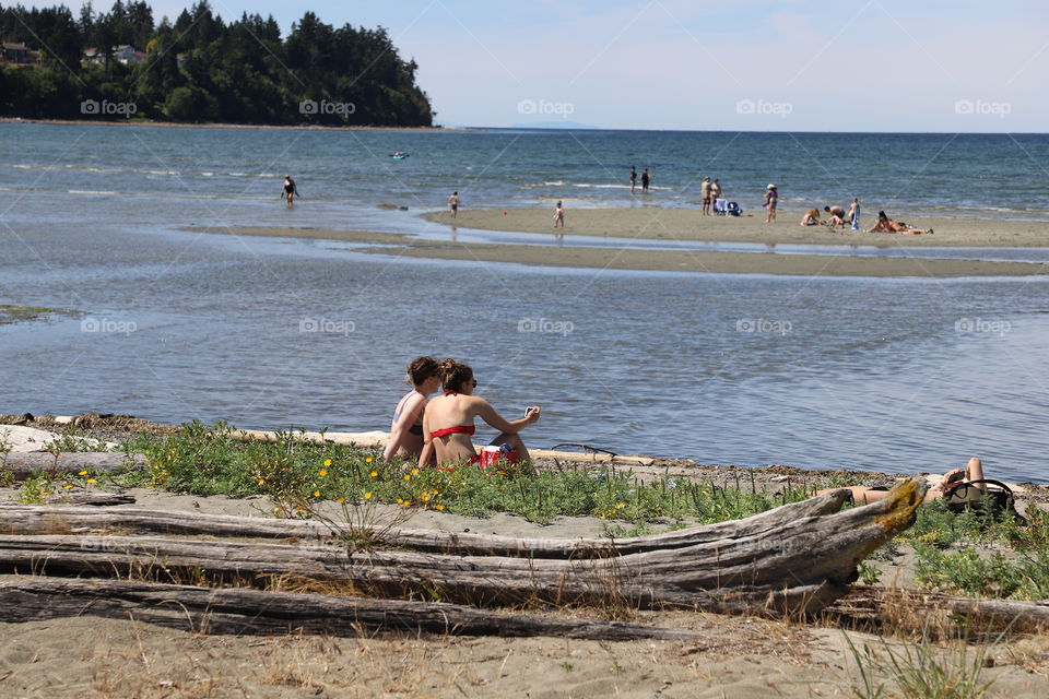 Girls sitting on the beach taking selfie and people on a sandy island made by low tide 