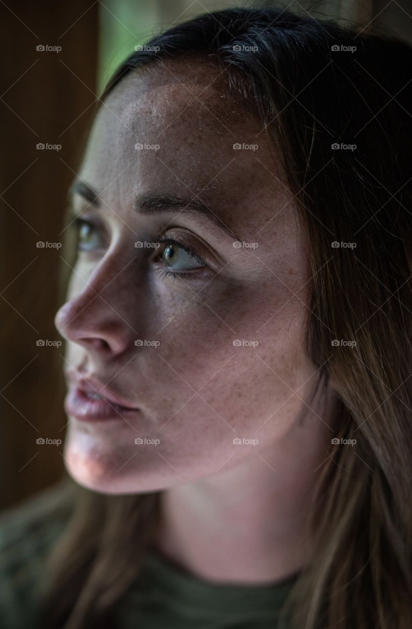 Picture of a girl looking out a window in soft light. She has green eyes that match her shirt. 