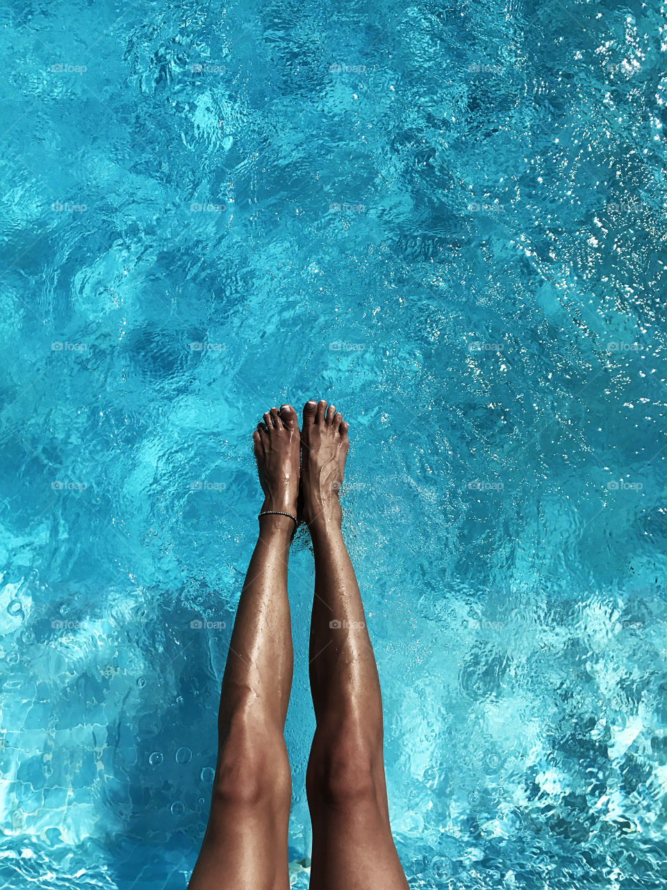 Tanned Female legs over the blue water of swimming pool 