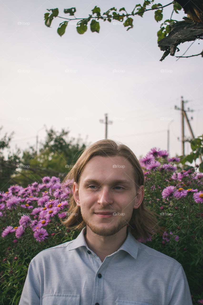 Portrait of a young man in the garden with purple flowers on the background. Soft evening light.