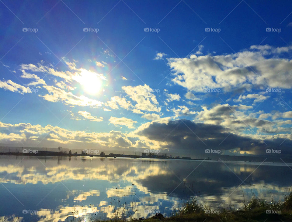 CLOUDS: Calm ocean water in this beautiful harbour on the West Coast provides a perfect mirror for the clouds backlit by the rising sun. A narrow sand spit in the background & some grass in the foreground provides some framing for the mirror.