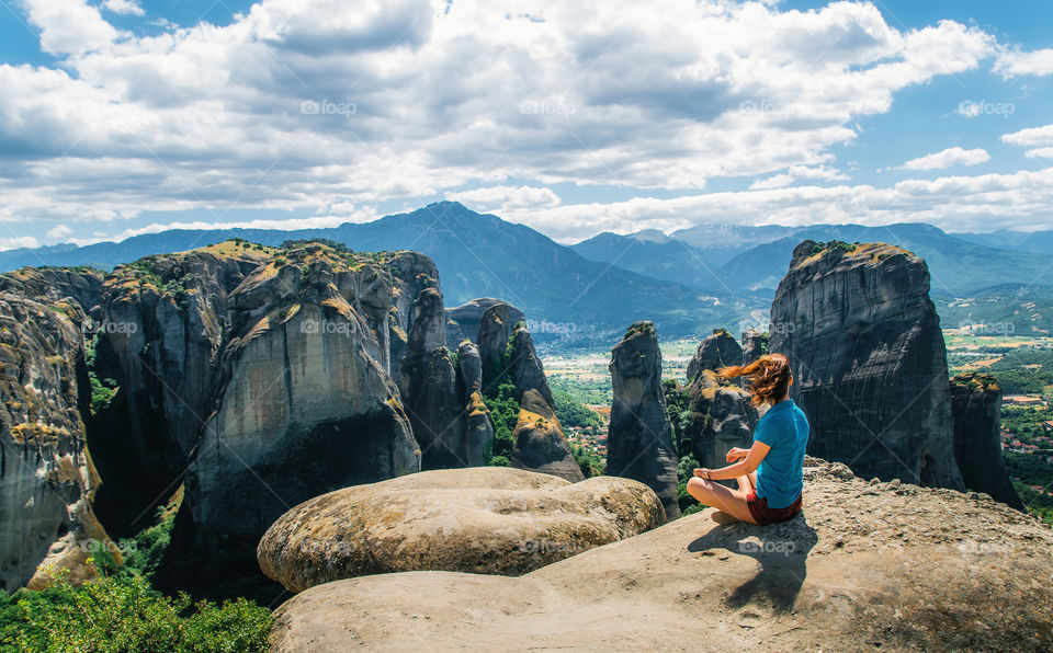 Young woman sits back to the camera on top of the mount and looks at the valley, Meteora, Greece