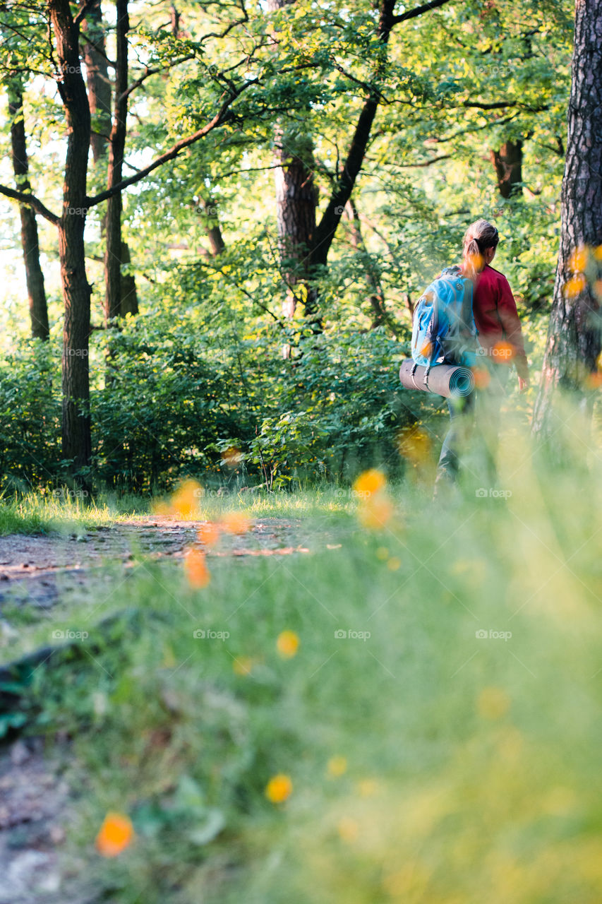 Young woman hiker with backpack walking along the path through the forest during summer vacation trip