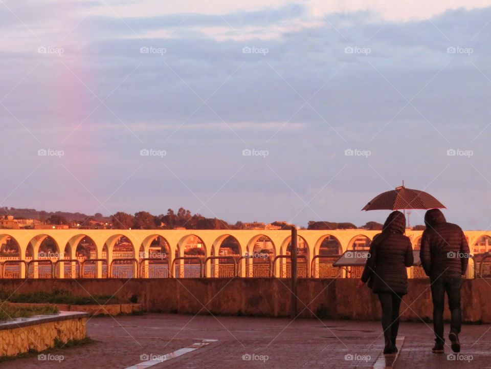 man and woman in a raining day at sunset with rainbow in the left side - Civitavecchia, Italy