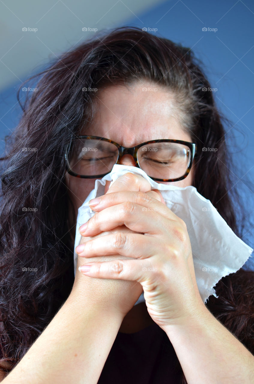 Woman blowing her nose hard into a tissue at home