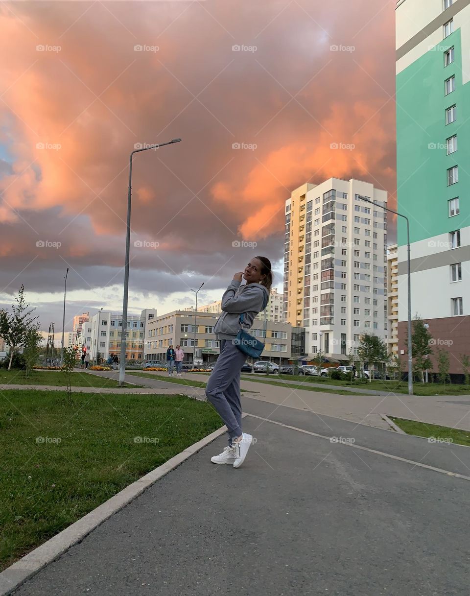 A young girl in a tracksuit walks around the city in front of a thunderstorm red clouds