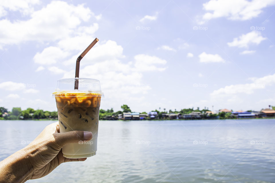 Hand holding a glass of cold espresso coffee Background views of the river and the home.