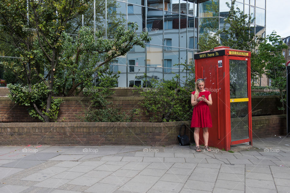 Woman 30 years old looking at her phone and social media at at WiFi spot at a telephone booth in London near Euston Square.