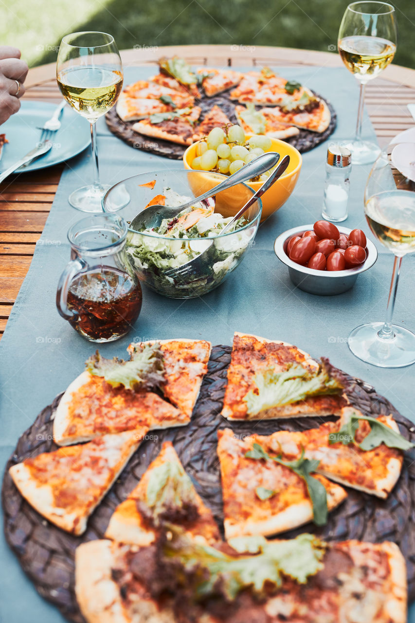 Dinner in a home garden. Pizza, salads, fruits and white wine on table in a orchard in a backyard