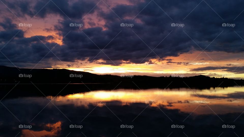 very dark dramatic Sunset with dramatic orange sky and clouds reflected in lake