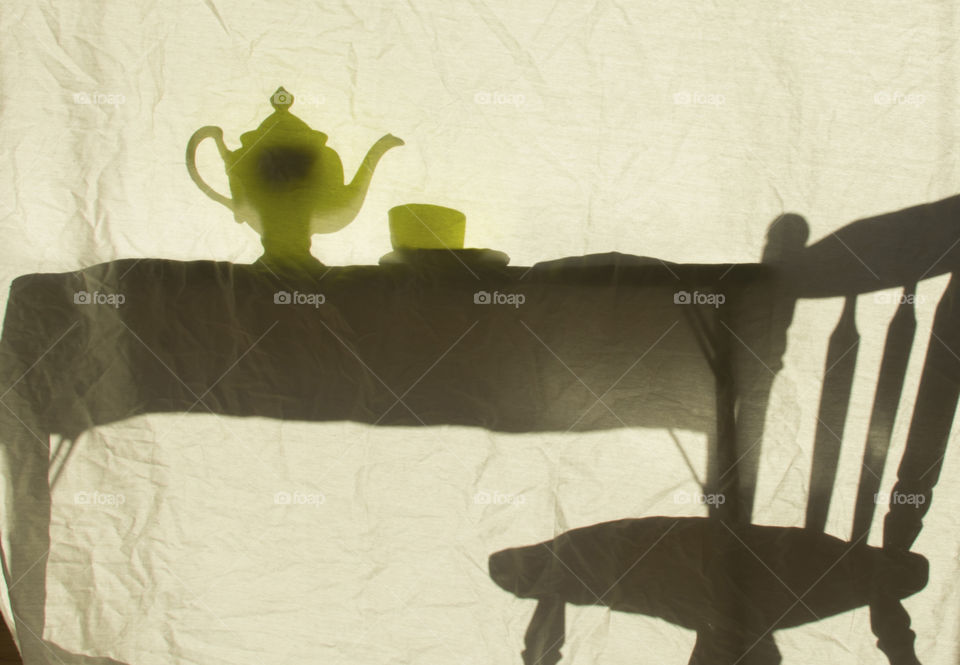 Silhouette of a table with a teapot and cup on it and a chair 