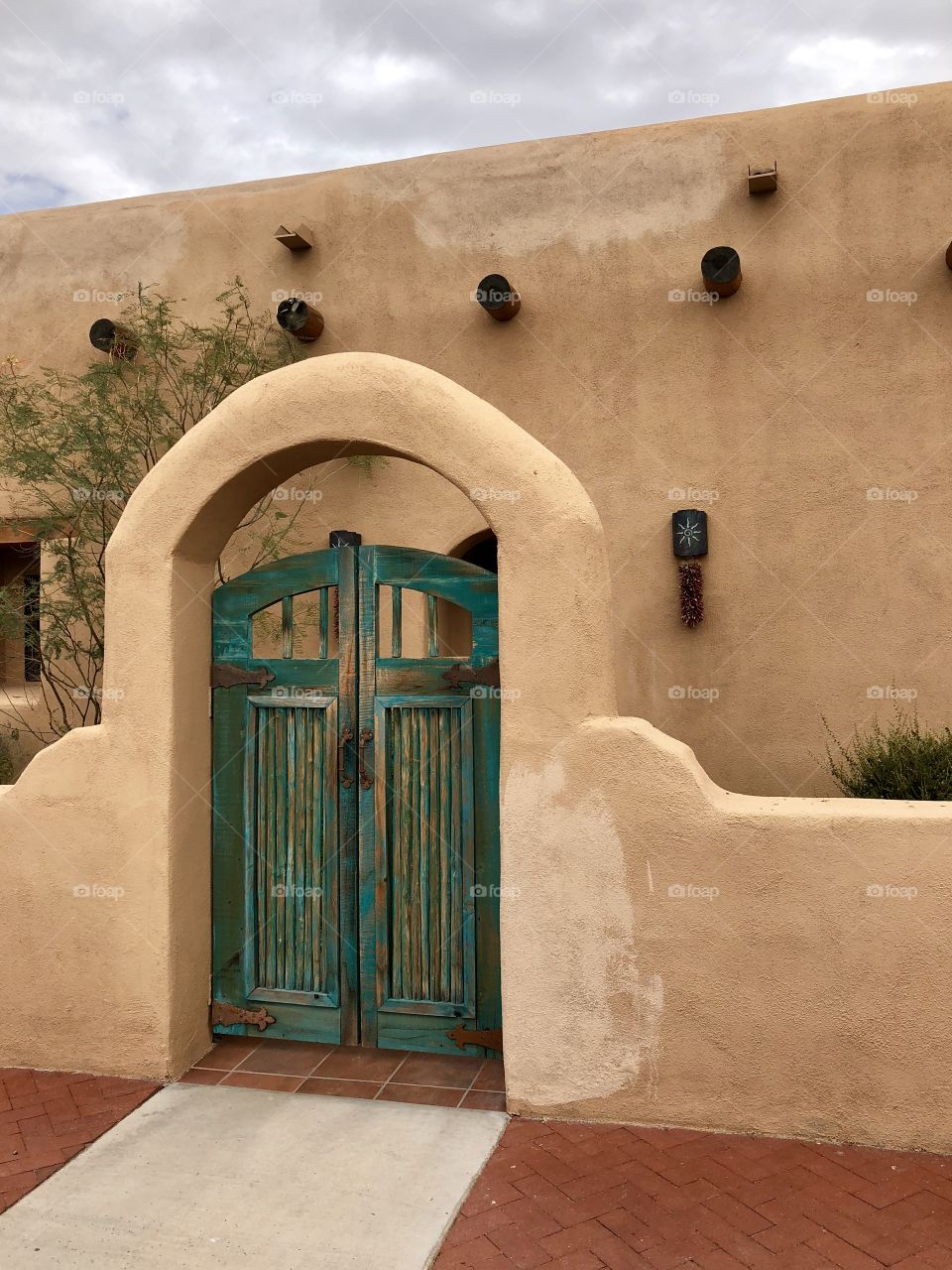 Rustic green doors to a courtyard of a brown adobe house