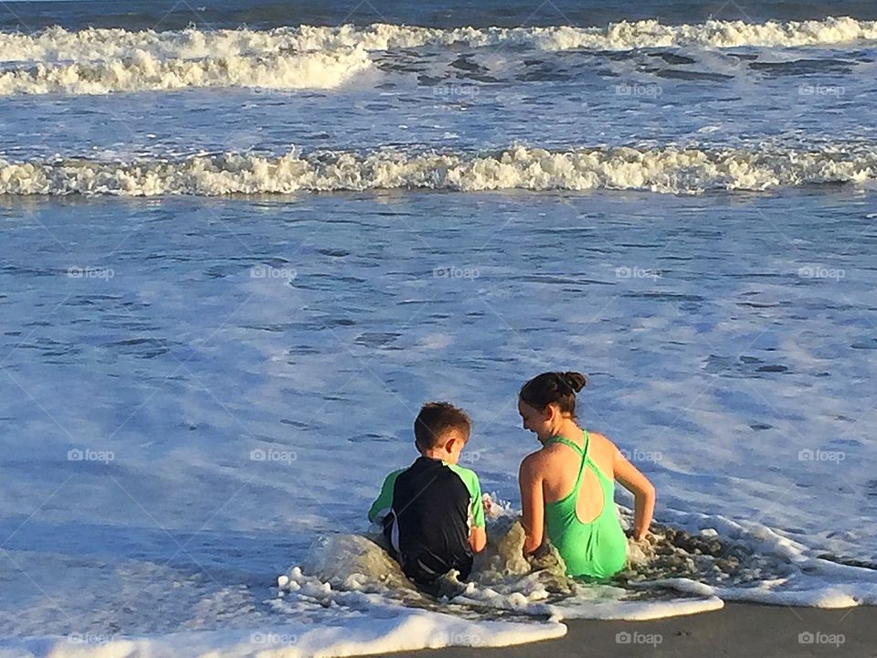 Boy and girl (siblings) enjoying the beach, tide, seashells