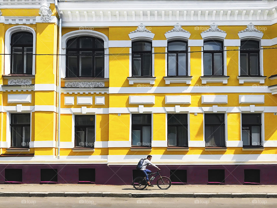 Young woman riding a bicycle and using mobile phone in front of the old yellow building in the city 