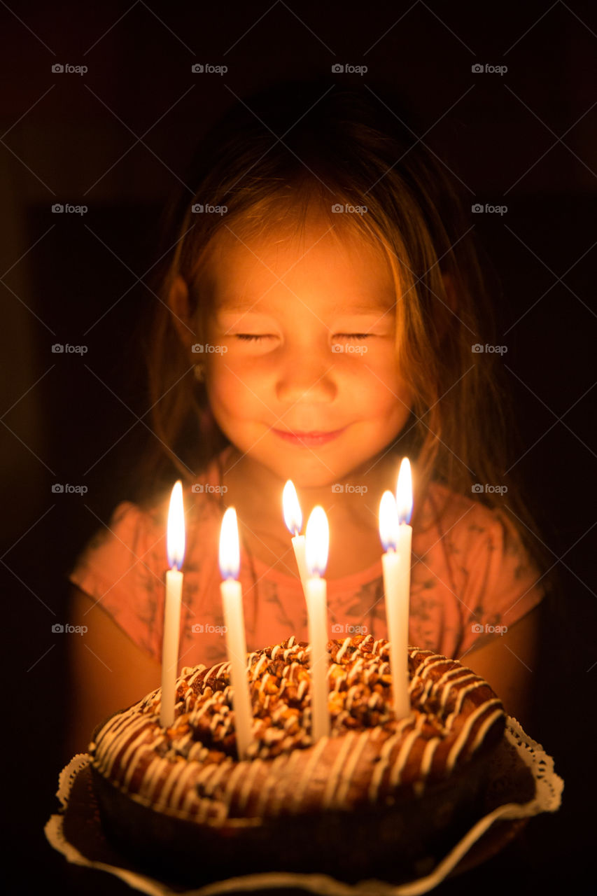 Close-up of girl with illuminated candle and cake