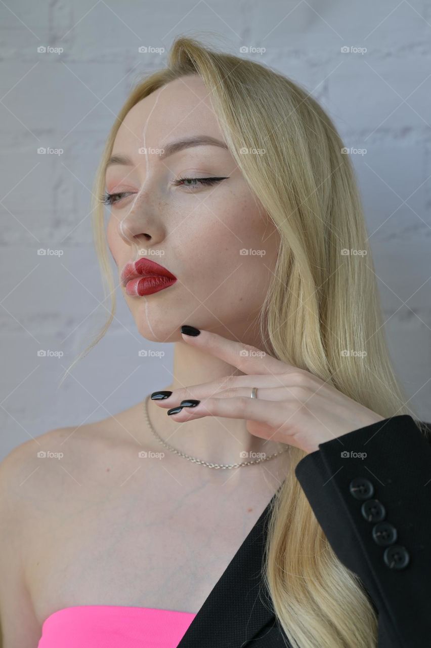 Close-up portrait of a blonde serious girl with different make-up on half of her face with her hand near her face on white background