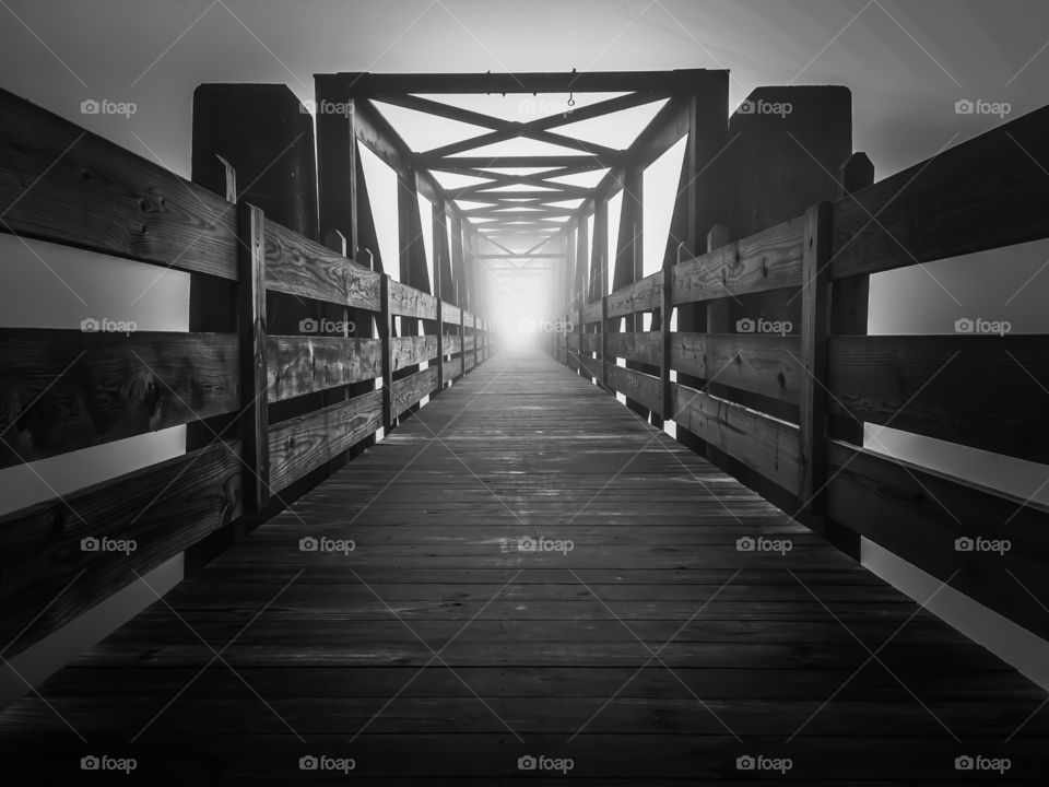 Black and white of an old truss footbridge vanishing into the fog. 