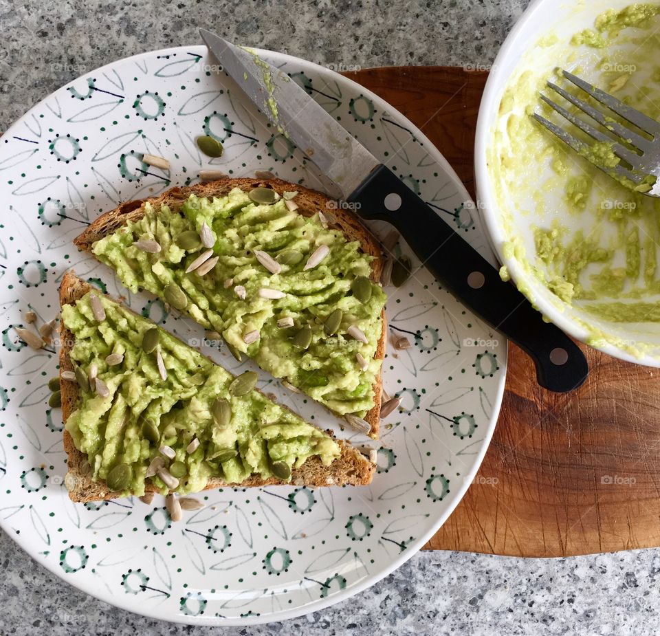 Avocado toast on seeded bread scattered with pumpkin and sunflower seeds and drizzled with olive oil