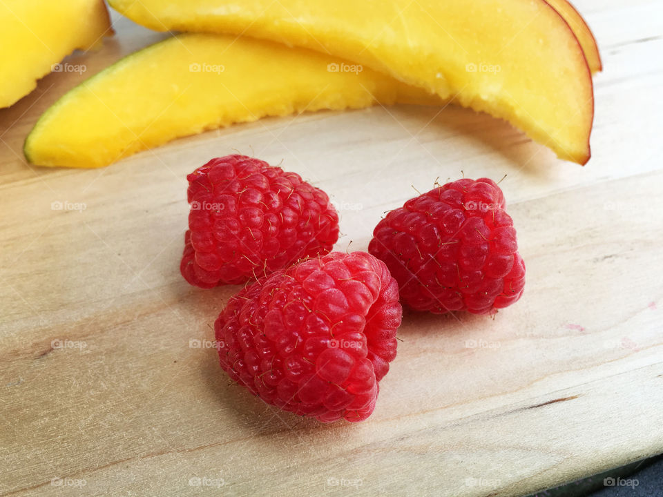 Fresh raspberries and mango slices arranged on a wood serving board